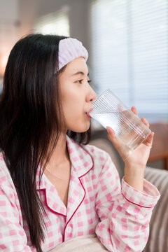 young Asian women drinking water glass morning routine after wake up wearing pink pajamas headband skincare beauty wellness healthy lifestyle home bedroom