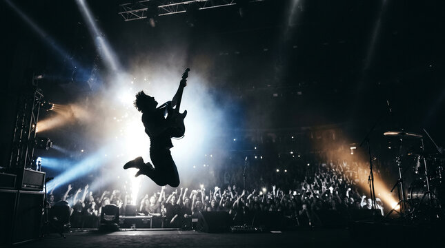 Musician silhouette jumping during guitar performance, high energy rock music moment, World Rock Day