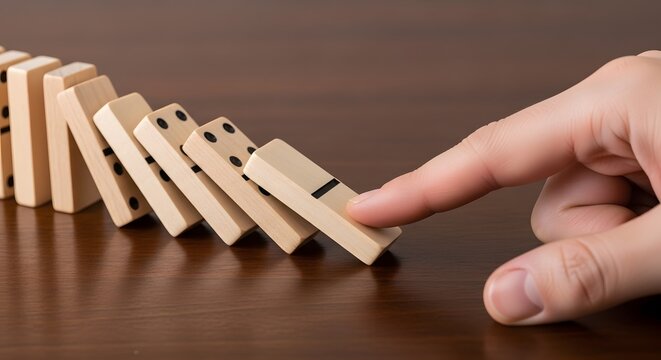 Hand pushing domino triggering a falling domino effect on wooden table