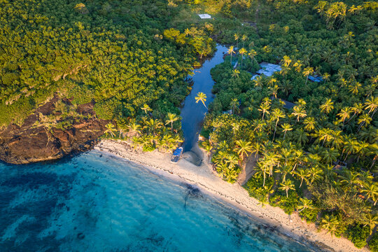 Aerial view of Yasawa Island featuring a pristine sandy beach, turquoise ocean water, and a dense palm tree forest under warm sunlight in Nadi, Western Division, Fiji.
