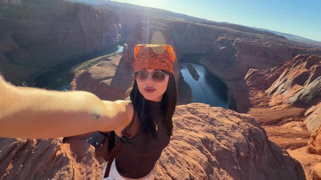 Stylish woman with a bandana filming herself while exploring the magnificent horseshoe bend in page, arizona, enjoying the breathtaking desert landscape and the colorado river on a sunny day