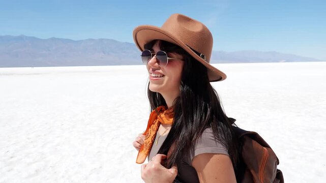 Young smiling woman with a backpack turning around and looking at the camera in a vast desert