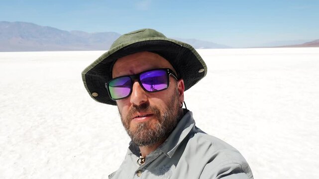 Young man with a beard vlogging with a selfie stick at Badwater Basin in Death Valley National Park