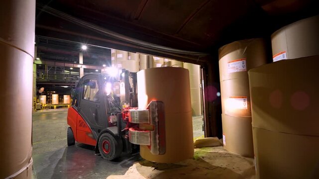 A forklift unloads and stacks paper rolls in a warehouse