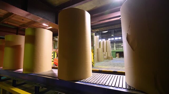 A forklift unloads and stacks paper rolls in a warehouse