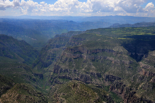 Aerial view of Barrancas del Cobre with its deep ravines, rugged rock formations, and lush green plateaus under a cloudy sky Chihuahua, Chihuahua, Mexico.