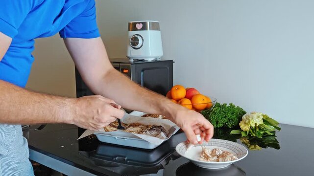 Man separating fish meat from salted fish on white plate, kitchen environment with microwave and fruit, home cooking process, culinary preparation.