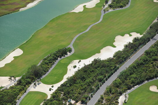 Aerial view of a lush golf course featuring green fairways, white sand bunkers, and a winding path alongside a turquoise water hazard in Cancun, Quintana Roo, Mexico.