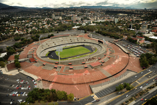 Aerial view of Estadio Olimpico Universitario featuring its green pitch and red concourse under a cloudy sky in Ciudad de Mexico, Ciudad de Mexico, Mexico.