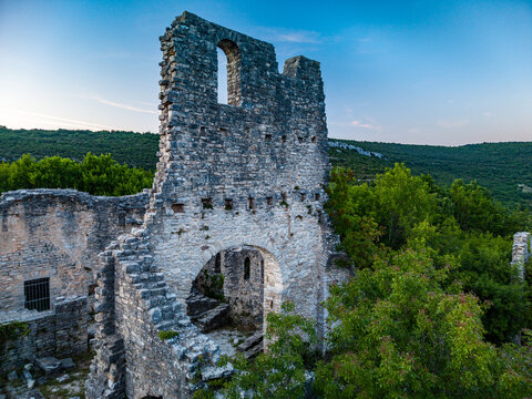 Aerial view of the ancient stone walls and arched windows of Dvigrad ruins surrounded by lush green forest and rolling hills in Kanfanar, Istria County, Croatia.