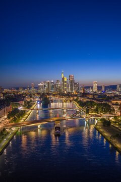 Aerial view of Flosserbrucke spanning the Main river with the illuminated skyline of the financial district under a twilight sky Frankfurt am Main, Hessen, Germany.
