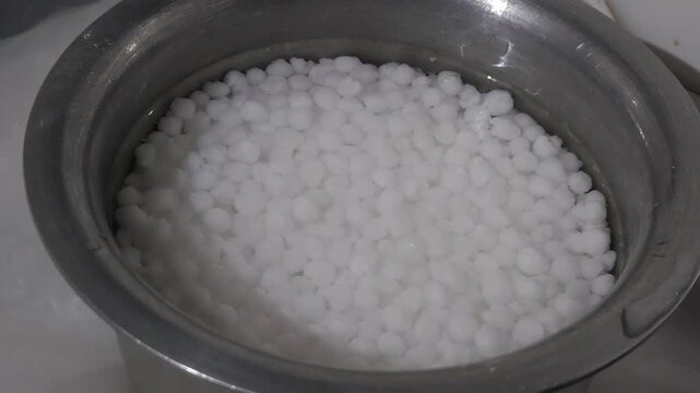 Soaking sabudana pearls in a steel bowl with water, prepared for cooking traditional Indian fasting recipes like khichdi or vada. Top view of tapioca sago balls being soaked for breakfast.