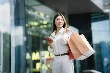Fototapeta premium Young woman carrying shopping bags outside a modern retail center, representing consumer lifestyle, fashion shopping, retail success, and urban spending trends.