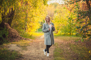 Fototapeta premium Smiling blonde woman walking autumn forest path, vibrant fall foliage, happy mood, natural light
