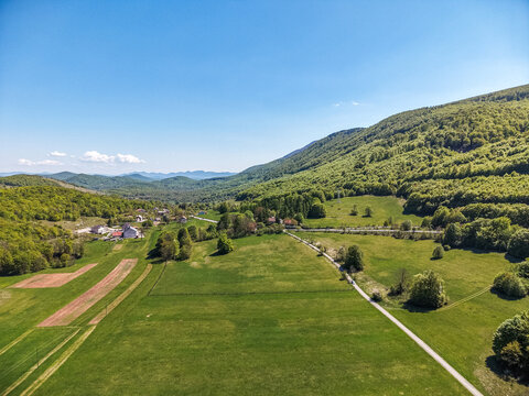 Aerial view of the Vratnik mountain pass featuring lush green hills, scattered houses, and a winding road under a clear blue sky Vratnik, Lika-Senj County, Croatia.