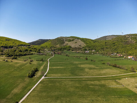 Aerial view of Vratnik mountain pass with wind turbines on the ridge and lush green fields under a clear blue sky Vratnik, Lika-Senj County, Croatia.