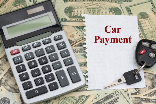 Car payment on a torn paper and car keys with calculator on twenty dollar bills for total costs of a auto
