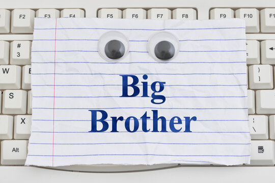 Big Borther text on ripped lined paper with googly eyes on a white computer keyboard for spying