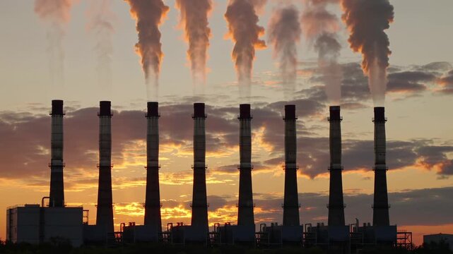 Industrial factory chimneys emit smoke against a dramatic sunset sky