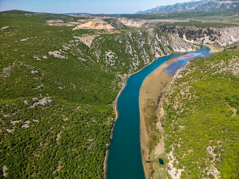 Aerial view of the winding Zrmanja River canyon with steep rocky cliffs and lush green vegetation under a clear blue sky near Zaton Obrovacki, Zadar County, Croatia.