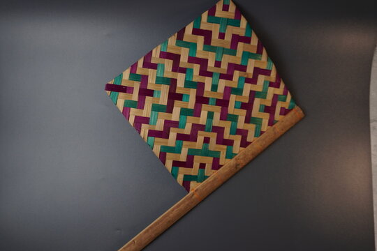 Traditional Indonesian woven bamboo hand fan isolated on a grey background. Colorful satay fan or kipas sate made from braided bamboo skin with geometric pattern, authentic cultural handicraft.