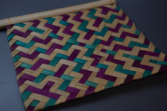 Traditional Indonesian woven bamboo hand fan isolated on a grey background. Colorful satay fan or kipas sate made from braided bamboo skin with geometric pattern, authentic cultural handicraft.
