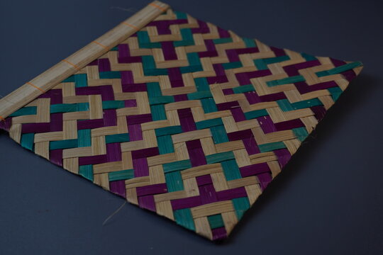 Traditional Indonesian woven bamboo hand fan isolated on a grey background. Colorful satay fan or kipas sate made from braided bamboo skin with geometric pattern, authentic cultural handicraft.