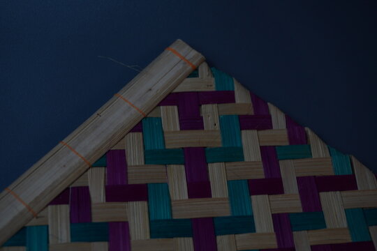 Traditional Indonesian woven bamboo hand fan isolated on a grey background. Colorful satay fan or kipas sate made from braided bamboo skin with geometric pattern, authentic cultural handicraft.