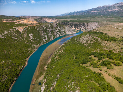 Aerial view of the Zrmanja river canyon winding through rocky hills and green vegetation under a clear blue sky in Zaton Obrovacki, Zadar County, Croatia.