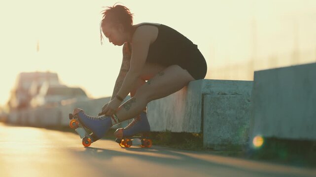 Tattooed woman tying laces on roller skates at sunset