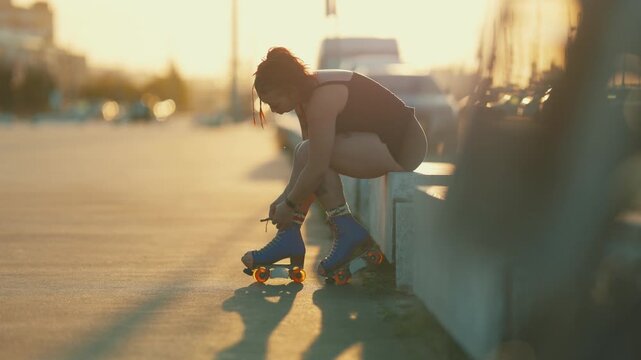 Young woman with tattoos tying roller skates at sunset