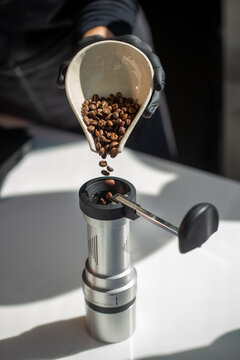 Barista pouring roasted coffee beans into manual hand grinder