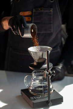 Barista pouring ground coffee powder into v60 dripper paper filter