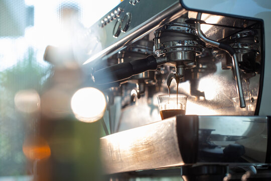 Espresso shot dripping from portafilter under warm sunlight flare