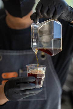 Barista pouring fresh brewed drip coffee from glass server into cup