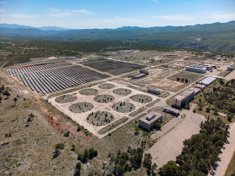 Aerial view of the Suncana elektrana Obrovac solar power plant and abandoned industrial buildings surrounded by green hills in Zaton Obrovacki, Zadar County, Croatia.