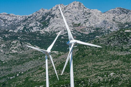 Aerial view of wind turbines standing against a backdrop of rugged limestone mountains and green vegetation in Zaton Obrovacki, Zadar County, Croatia.