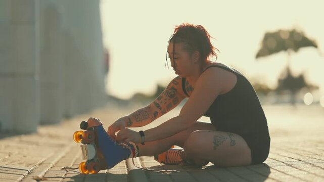 Tattooed woman lacing up roller skates at sunset