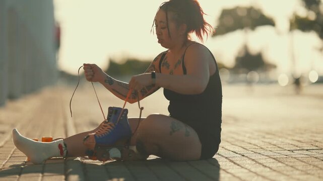 Tattooed asian woman untying roller skates outdoors