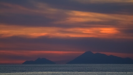 Fototapeta premium View of mountains in the middle of the sea with black and orange sky.