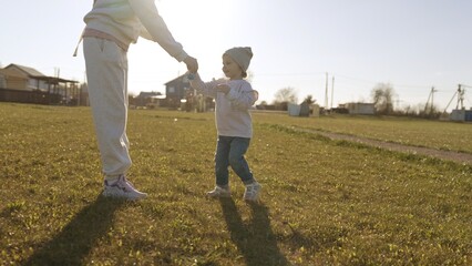 Obraz premium Mother and daughter holding hands, walking through sunlit green field on a warm spring day, sharing playful bonding, joy and quiet connection in the countryside