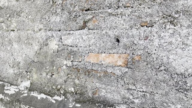 Close up of damaged concrete wall revealing red brick layer