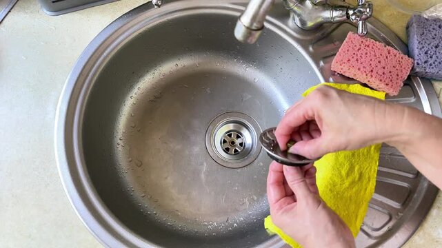 Female hand puts metal drain strainer into kitchen sink. Person installs steel plug in silver sink bowl. Domestic housework involves cleaning sink drain for hygiene at home with hand.