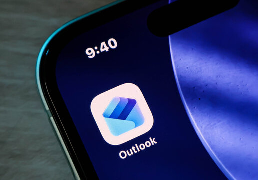 Closeup of a smartphone screen displaying the microsoft outlook app icon with a blue gradient design on a dark background