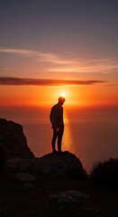 Obraz premium Silhouette of a person standing on a rock against a vibrant sunset sky