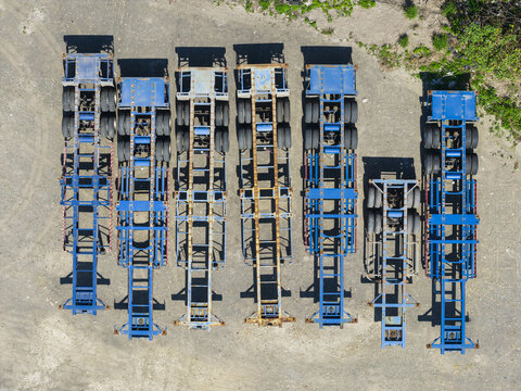 Aerial view of several blue semi-trailer chassis parked in a row on a gravel lot with green vegetation in Taiwan.