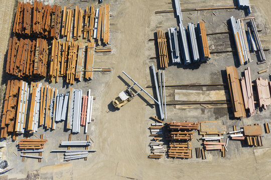 Aerial view of industrial steel beams stacked in a construction yard with a forklift moving materials on the ground in Taiwan.