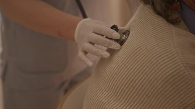 Close up anonymous paramedic using stethoscope while performing auscultation, listening to senior womans lungs