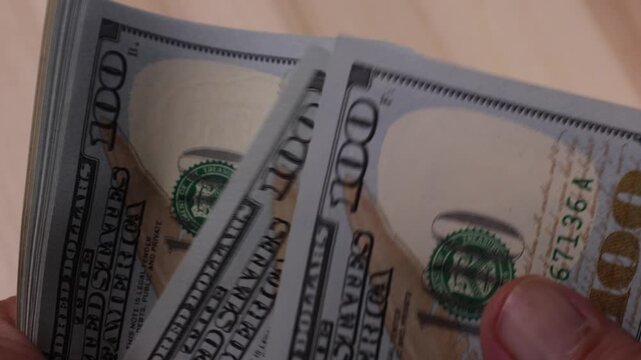 Detailed close-up footage showing hands rapidly counting multiple US dollar bills, capturing texture and motion of the currency in bright lighting.