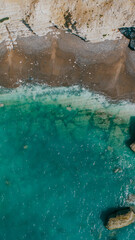 Fototapeta premium Aerial top-down view of turquoise sea and sandy beach below cliffs